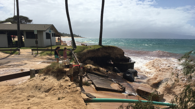 Two passersby walking a dog look at a decommissioned cesspool and other infrastructure exposed by beach erosion at Kapukaulua (Baldwin Beach Park, Maui, Hawaii) in September 2016.