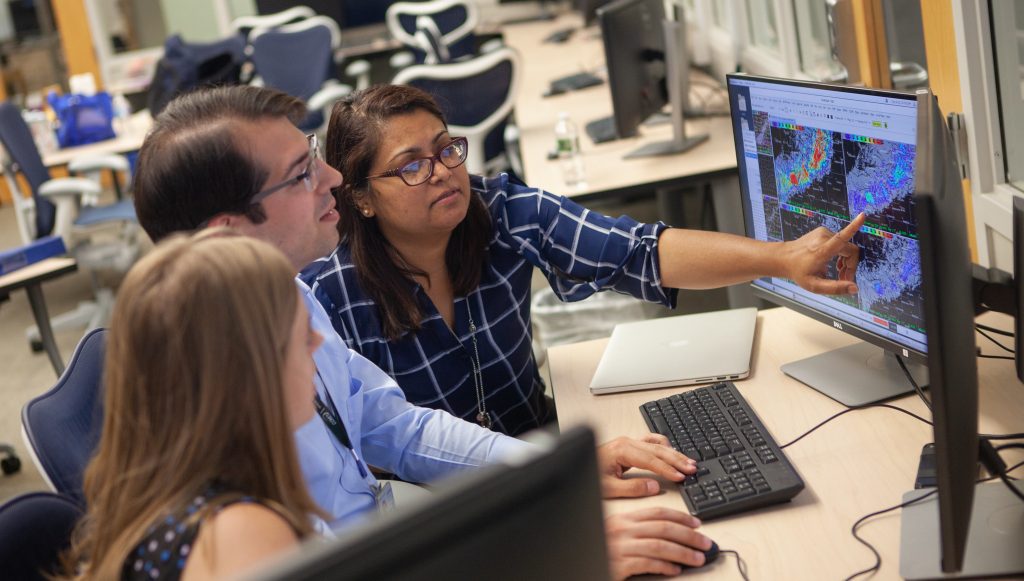 Photo of three researchers/forecasters working together at a computer to improve weather products and services.