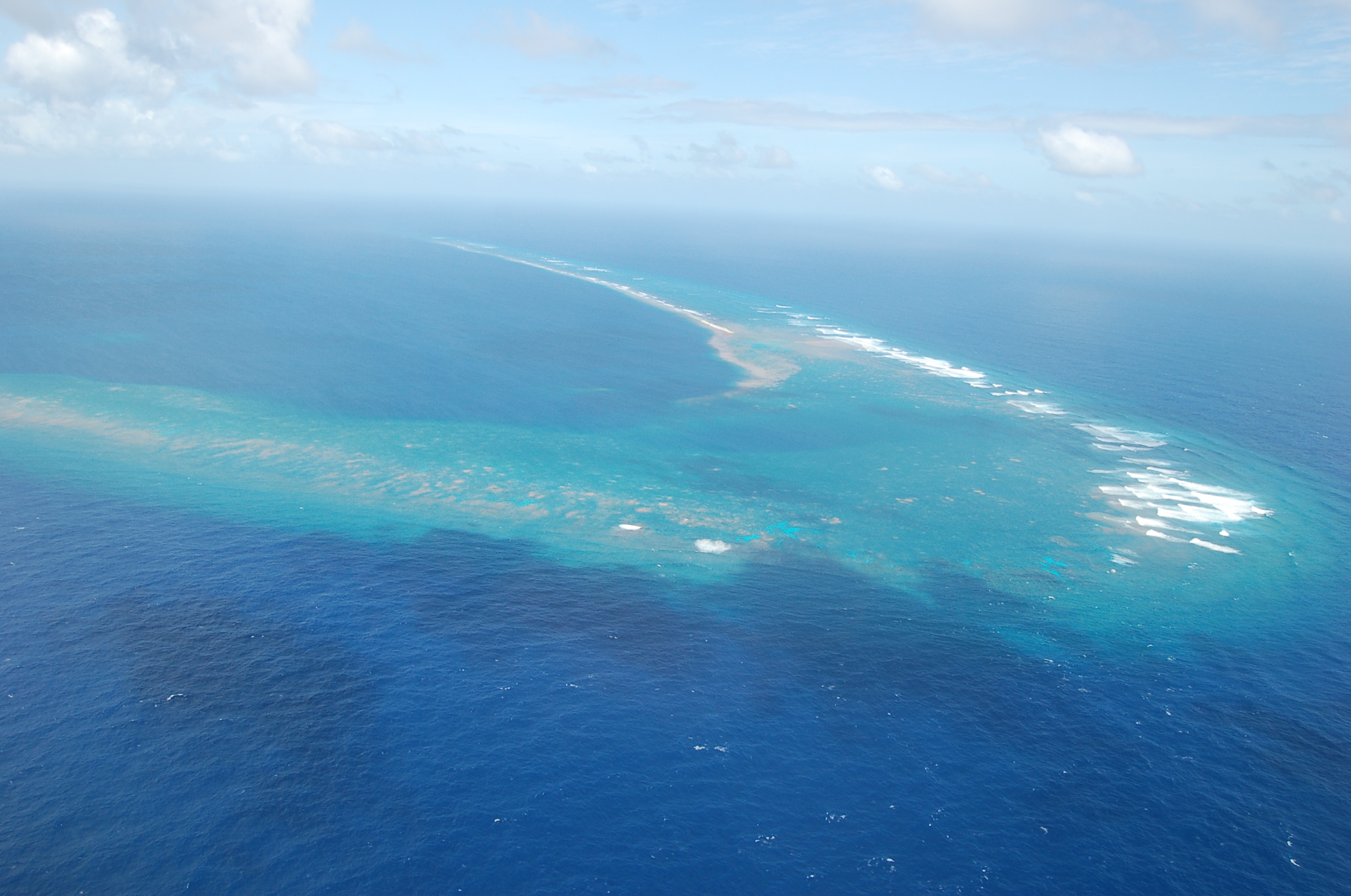 Aerial view of Kingman Reef National Wildlife Refuge. With less than five feet of elevation in most areas, Kingman Reef remains one of the most pristine coral reef atoll ecosystems in the Pacific Ocean. Located 932 miles southwest of Hawaiʻi, the crystal clear waters and vibrant corals support a spectacular diversity of algae, fish, marine mammals, sea turtles, and migratory birds.