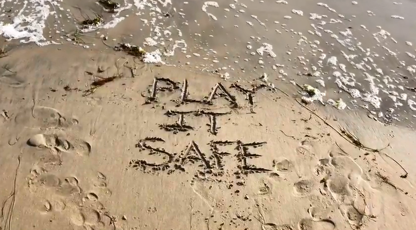 Play it safe written in the sand at a beach.