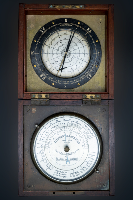 A barocyclonometer, lying open. There are two faces with dials. On the bottom a barometer and on the top a cyclonometer.