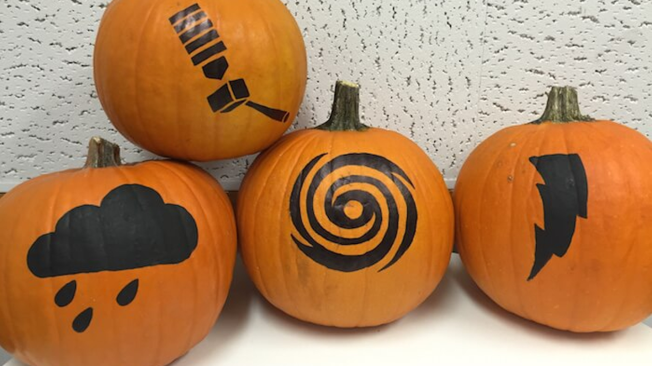Four pumpkins with painted art including a satellite, a cloud, a hurricane, and a lightning bolt.