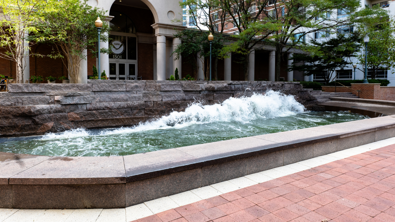 Photo of the “Coastline” wave pool art installation outside NOAA’s Silver Spring, MD campus. Waves crash against a rough stone wall in a long rectangular pool.