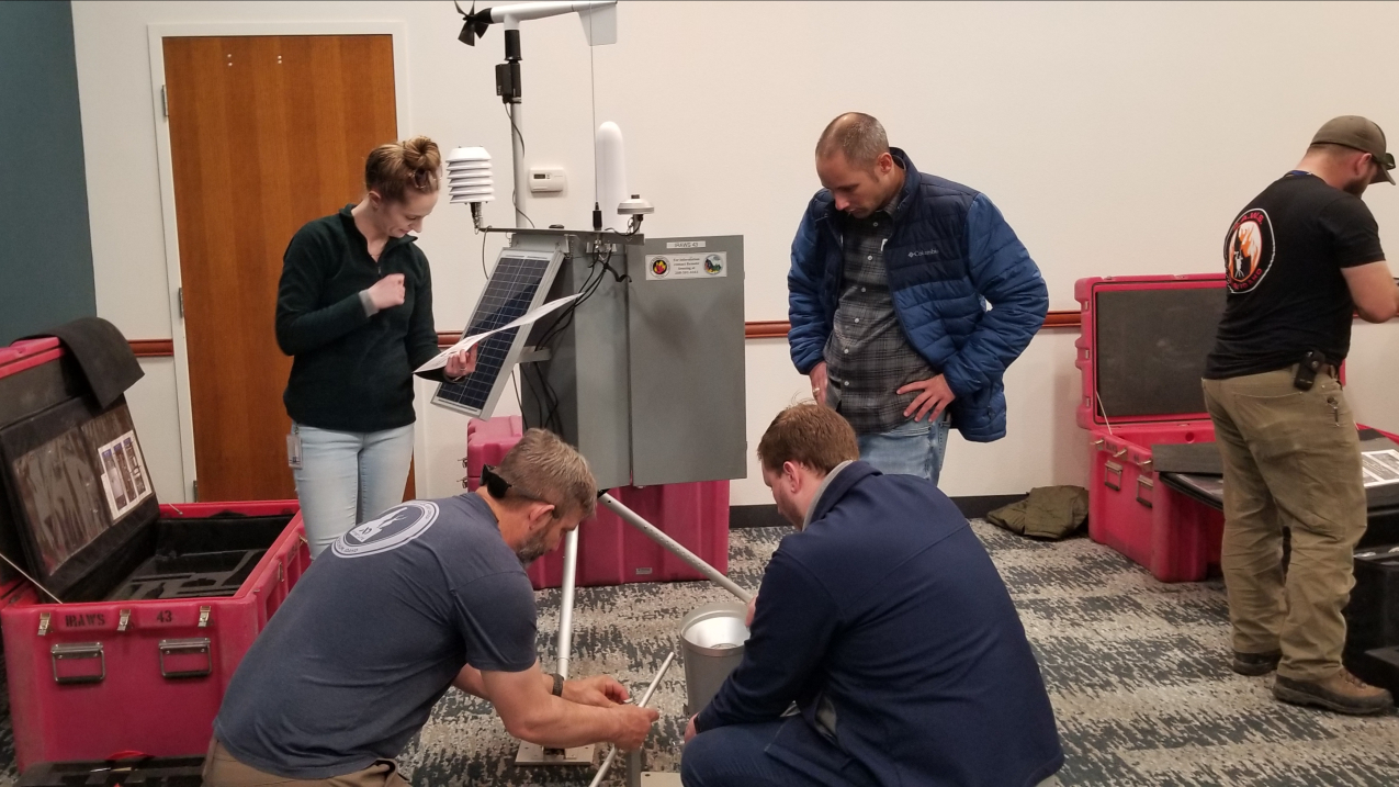 Photo of IMETs learning how to set up an Incident Remote Automatic Weather Station (IRAWS). IRAWS gather observations useful for fire weather forecasting including wind speed and direction, air temperature, precipitation, relative humidity, solar radiation and fuel moisture.