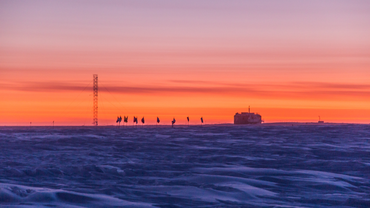 Early colors of a rising sun approach the horizon behind NOAA's Atmospheric Research Observatory at the Amundsen-Scott South Pole Station, September 8, 2018. 