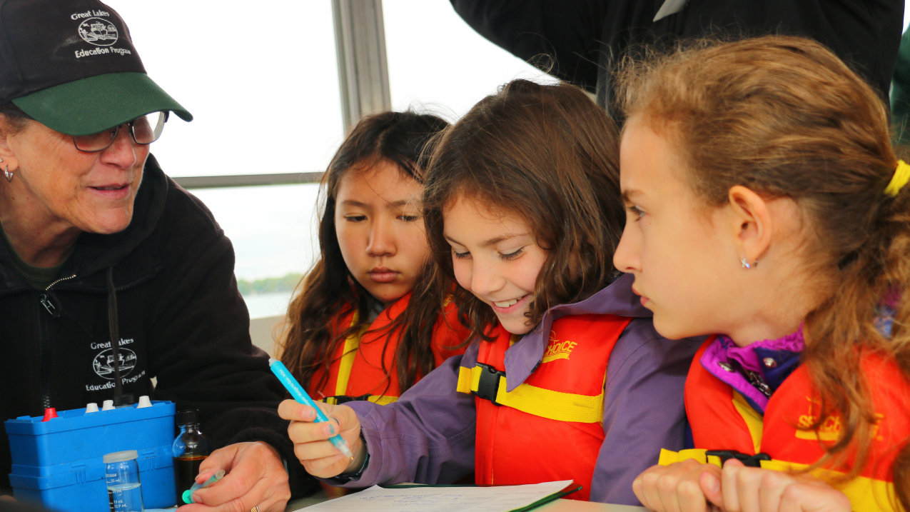 Three elementary aged students and an instructor work with information on a clipboard.