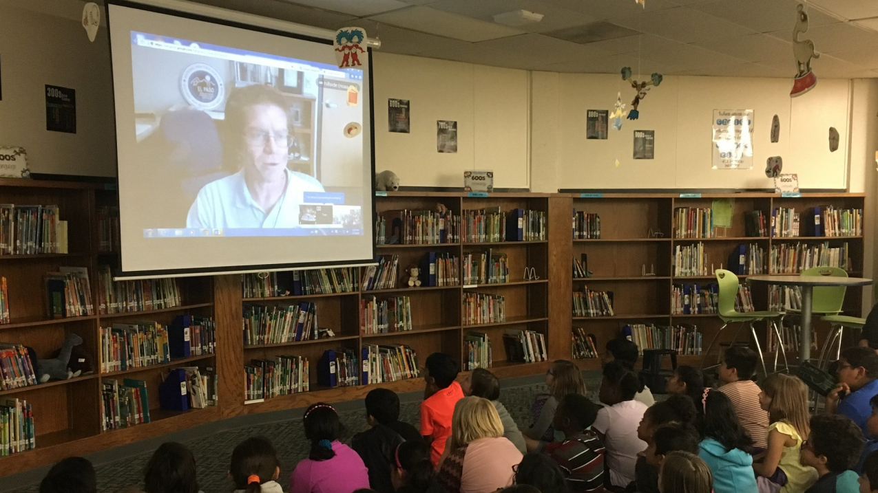 Seated in a school library, third-grade students from Illinois ask National Weather Service forecaster Tim Brice their weather questions via video conference.
