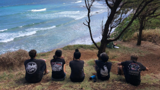 Five students sit along the ocean coast and stare out into the water.