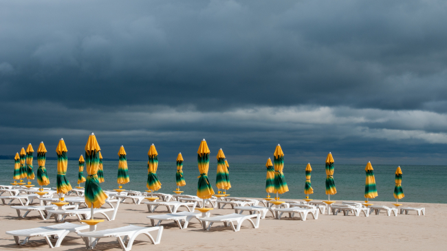 Closed umbrellas on a beach with a storm approaching
