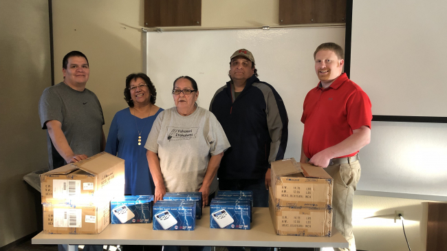 Four representatives of the Fort Peck Indian Reservation and a National Weather Service employee stand behind a table filled with boxes of NOAA Weather Radios.