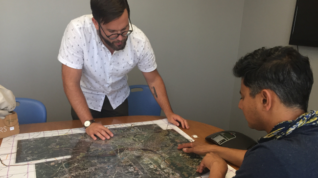 Jeremy Hoffman and Vivek Shandas closely examine a large map with highly detailed satellite images of a city.