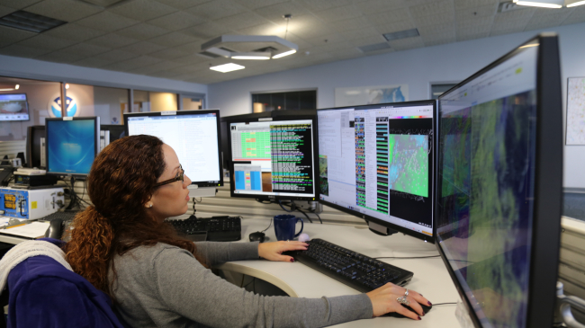 forecaster seated and working at a bank of four computer screens
