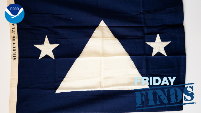 The flag of U.S. Coast and Geodetic Survey Director Rear Admiral Lee Otis Colbert. It is a blue field with a large white equilateral triangle in the center and two smaller stars on either side. The hoist has two brass grommets and is marked “DIRECTOR.FLAG. NO 2.”