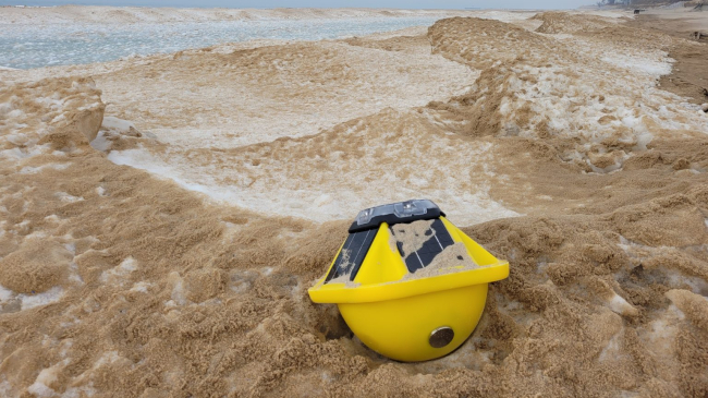 Winter-ready buoy on the ice, surrounded by sand from the shore of Lake Michigan.