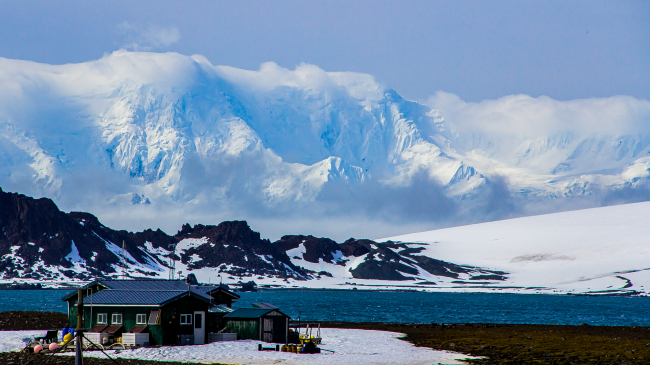The tiny Antarctic field camp at Cape Shirreff on a sunny day and bluish skies with tall, snowy Antarctic mountains in the background.