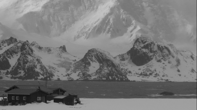 A black and white image of a tiny Antarctic field camp settled among huge, snow-covered mountains of Cape Shirreff.