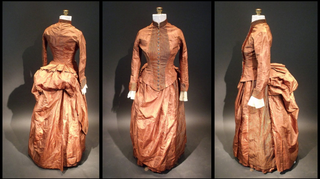 Three photos of the 1880s silk bustle dress in which crumpled bits of paper containing a code were found. The back, front, and left side are shown in a triptych. The dress  is a deep peach color with a striped placket on the front and a large bustle. The pocket where the code was found is located under the overskirt at the right hip.