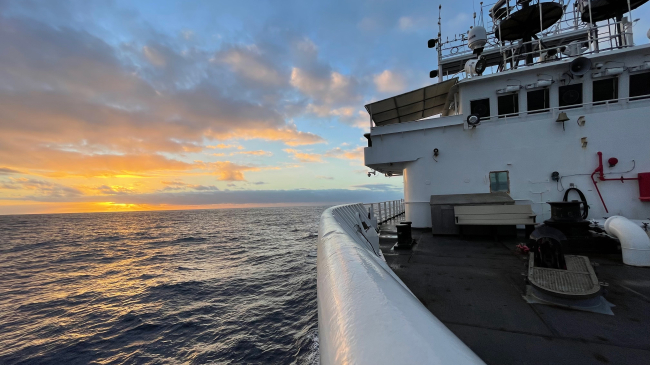 Photo showing Sunset from the bow of NOAA Ship Okeanos Explorer on Day 8 of the EXPRESS: West Coast Mapping 2022 expedition illuminates calming seas and a smoother ride. Image courtesy of NOAA Ocean Exploration, EXPRESS: West Coast Mapping 2022.