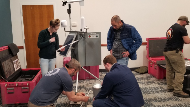 Photo of IMETs learning how to set up an Incident Remote Automatic Weather Station (IRAWS). IRAWS gather observations useful for fire weather forecasting including wind speed and direction, air temperature, precipitation, relative humidity, solar radiation and fuel moisture.