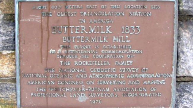 Photo of a plaque that reads, "About 600 meters East of this location lies the oldest triangulation station in America, Buttermilk 1833, Buttermilk Hill, This plaque is established as a bicentennial commemoration through the cooperation of: The Rockafeller Family, The Nation Geodetic Survey of National Oceanic and Atmospheric Administration, American Congress on Surveying and Mapping, The Westchester-Putnam Association of Professional Land Surveyors, Incorporated, 1976"