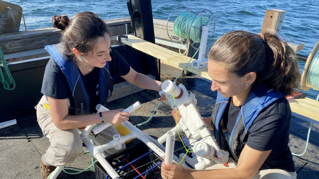 Photo showing Ocean Discovery Director of Engineering Jessica Sandoval, Ph.D., (left) and Ocean Discovery League President and founder Katy Croff Bell, Ph.D., (right) work on attaching a low-cost camera system and light modules to a prototype weighted lander configuration made of PVC pipe during deployment and recovery trials in the waters off Rhode Island. Accessible deployment and recovery systems are critical to the development of low-cost deep seas systems. Credit: Susan Poulton/ Ocean Discovery League.