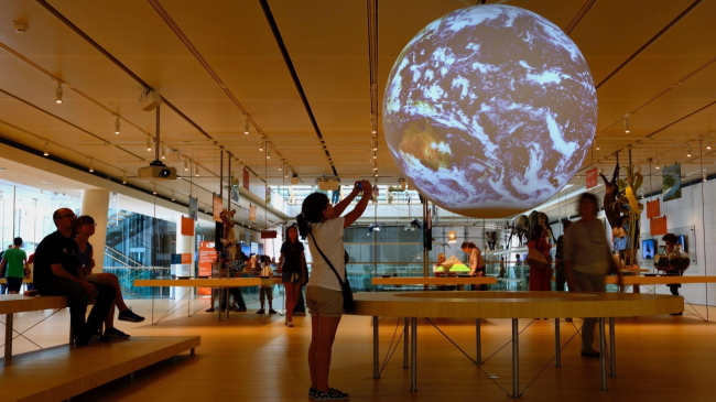 A young girl takes a photo of a 6-foot animated globe showing a color view of the Earth with clouds of the globe at a museum exhibit.