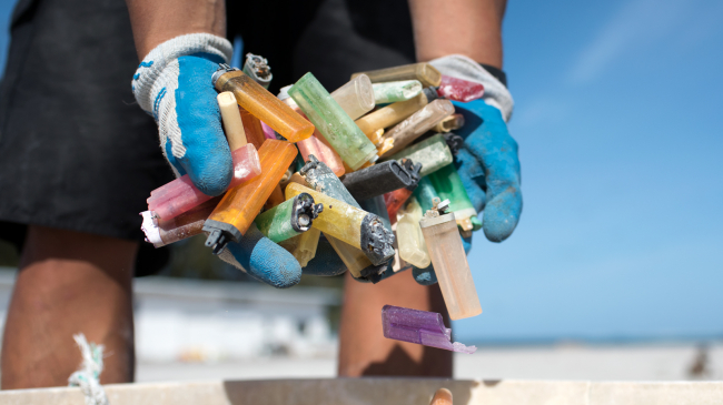 A marine debris team member gathers a handful of disposable cigarette lighters picked up at a beach cleanup site.