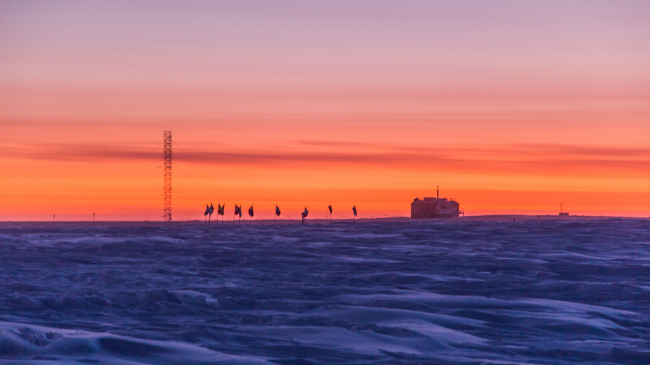 Early colors of a rising sun approach the horizon behind NOAA's Atmospheric Research Observatory at the Amundsen-Scott South Pole Station, September 8, 2018. 