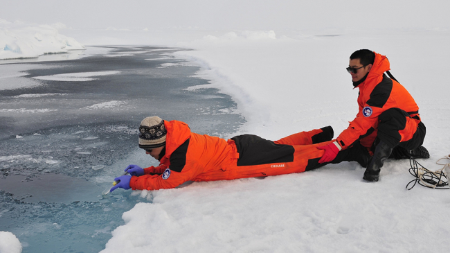 University of Delaware researcher Baoshan Chen (pictured left) takes water samples from a melting pond on ice in the northern Arctic Ocean basin with a Chinese collaborator.