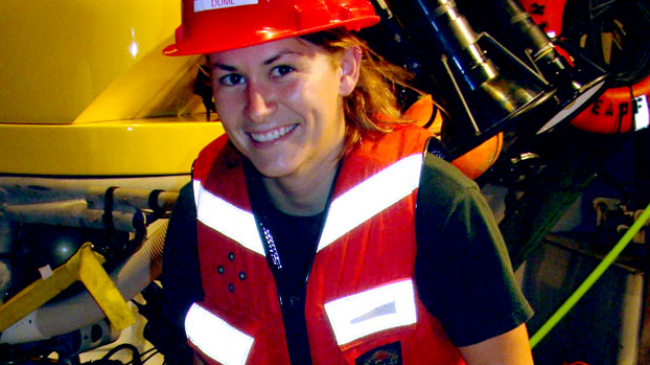A biologist on a ship wearing a protective helmet and a reflective vest.