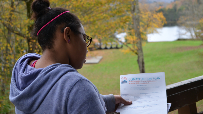 A student looks at papers while standing on an outdoor balcony.
