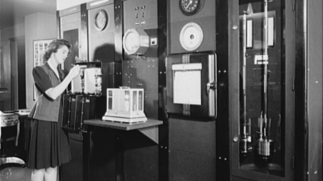 A woman in the Weather Bureau station at National Airport (Washington, DC) is gathering surface weather observations at a Weather Bureau instrument panel on which are mounted barometers, thermometers, wind direction and velocity indicators, and other instruments for measuring weather elements, circa 1943.