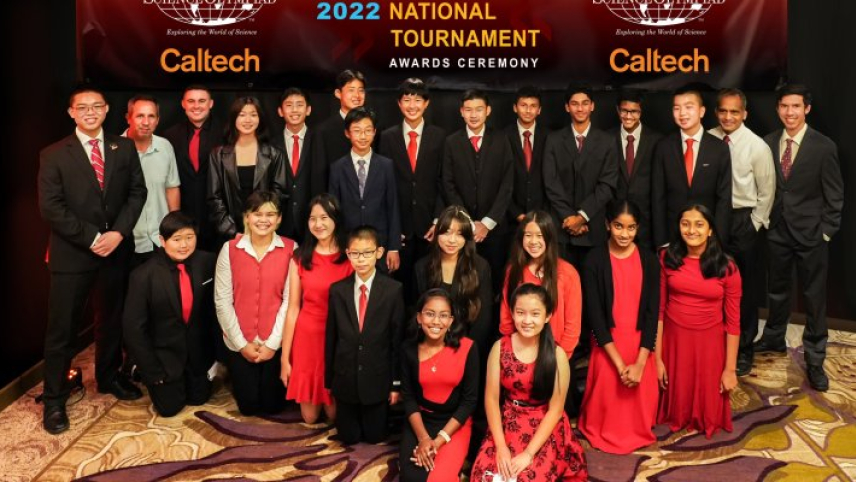 A group of students wearing their school colors (red and black) stand in front of a large Science Olympiad Caltech banner.