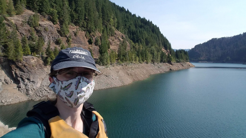 Chrissy wears a fabric mask with fish on it and stands in front of a mountain range.