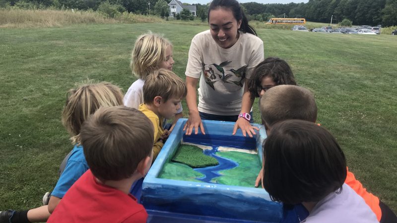 Sophia Troeh (middle), a 2018 NOAA Hollings scholar, explains the importance of salt marshes in estuarine systems and the impact humans have on rivers, oceans, and estuaries through runoff. This took place at the Wells Estuarine Research Reserve in Wells, Maine, in August 2019.
