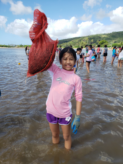 A Sacred Hearts student holds up a bag full of invasive algae she removed from Maunalua Bay. On November 9, 2018, this student and 54 of her classmates got knee-deep in their nearshore habitat to pull invasive algae and learn about its impact on the surrounding ecosystem.