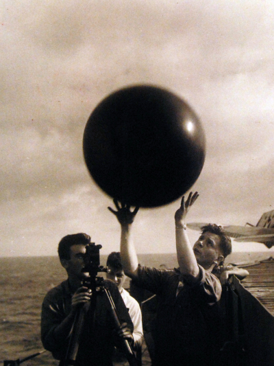 A black and white photo of Navy sailors releasing a weather balloon into the air from a ship.