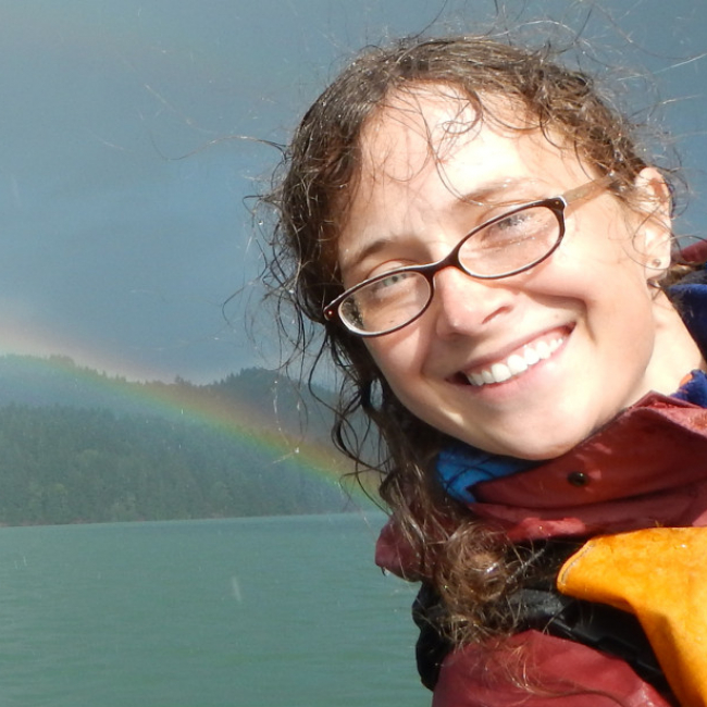 Chrissy smiles on a boat with a rainbow in the background
