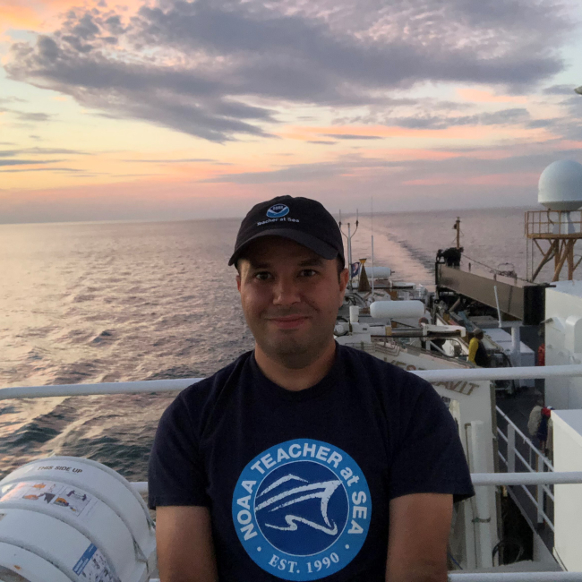 Oktay Ince poses on NOAA Ship Thomas Jefferson with a view of Lake Erie behind him. 