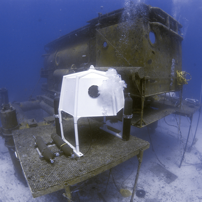 This photo shows the NOAA Aquarius, a blocky, rectangular undersea habitat. A platform outside the Aquarius holds a smaller structure.