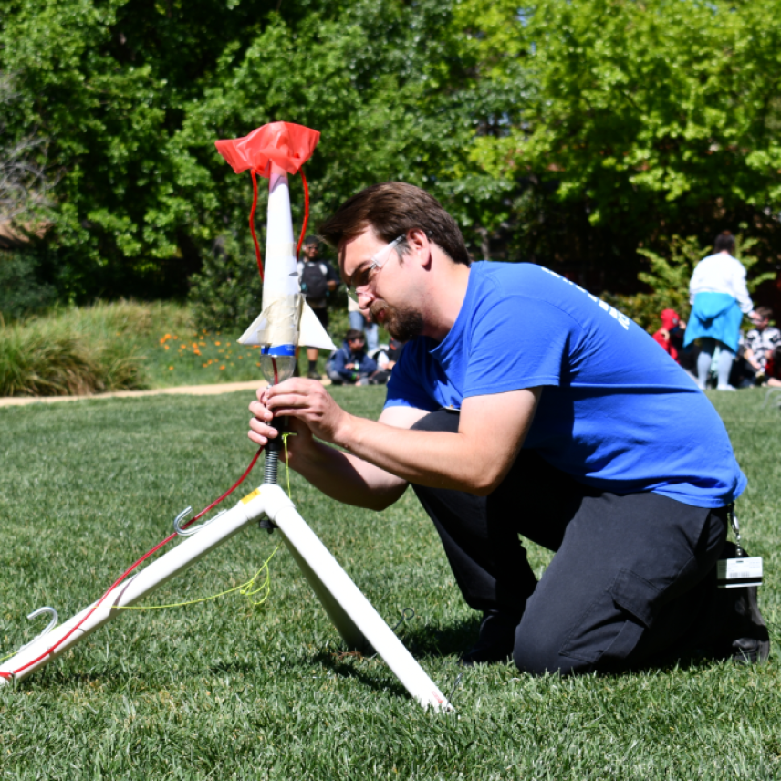 Cole leans down on grass lawn and adjusts a model rocket.