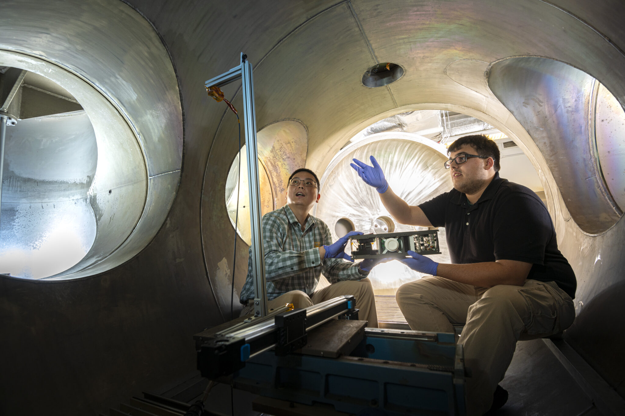 Dr. Daoru Han, left, and Jacob Ortega discuss engineering techniques inside a plasma vacuum chamber. Han and Ortega are working with a group of undergraduate researchers on a NASA challenge. Photo by Michael Pierce/Missouri S&T.