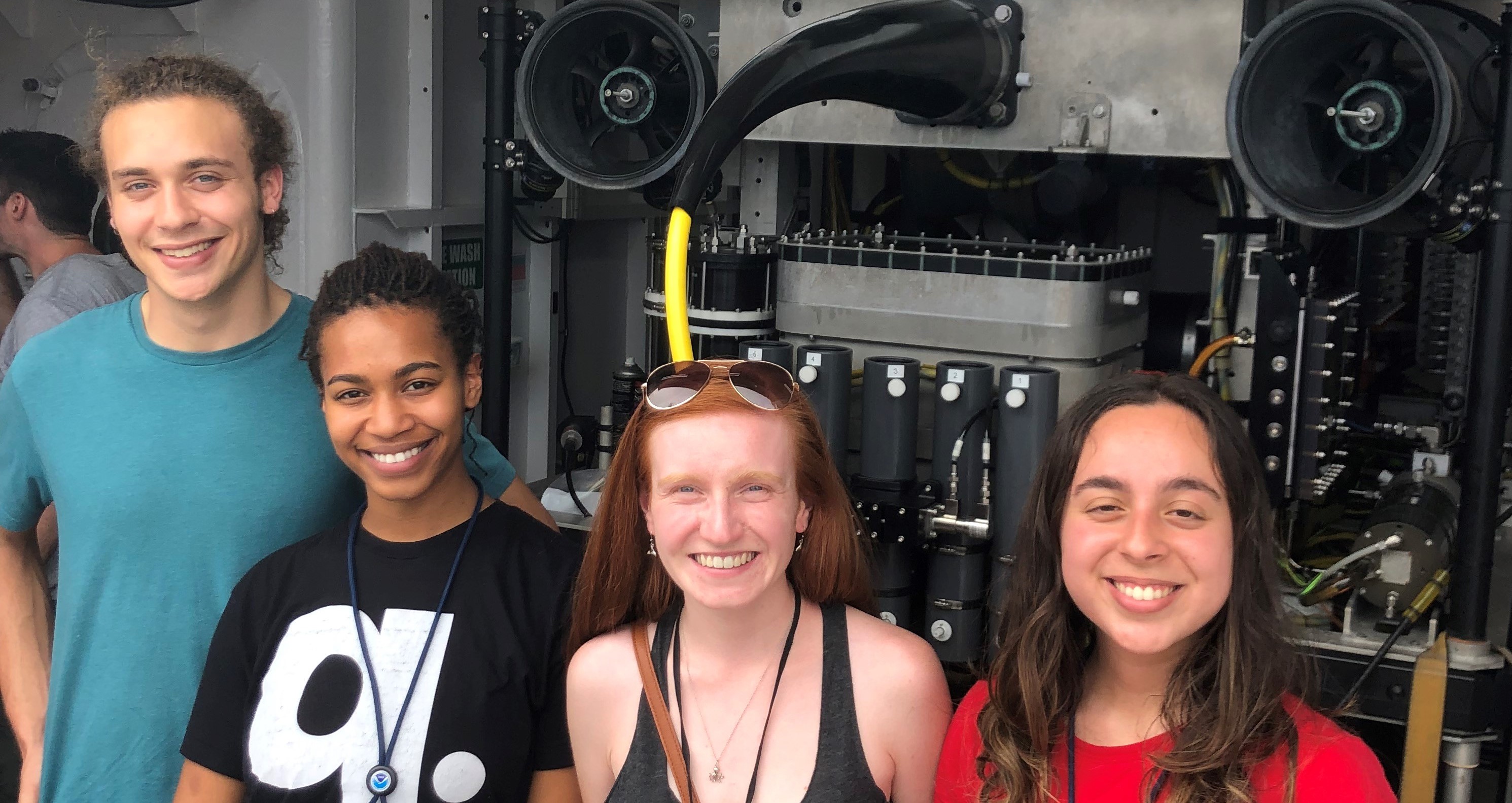From the left, Herbert Leavitt (2018 Hollings scholar), Kristyn Wilkerson (2019 EPP/MSI scholar), Laura Anthony (2018 Hollings scholar), and Paola Santiago (2019 EPP/MSI scholar) aboard NOAA Ship Okeanos Explorer standing in front of the ROV Deep Discoverer after its return to port from the Windows to the Deep 2019 Exploration of the Mid and South Atlantic.