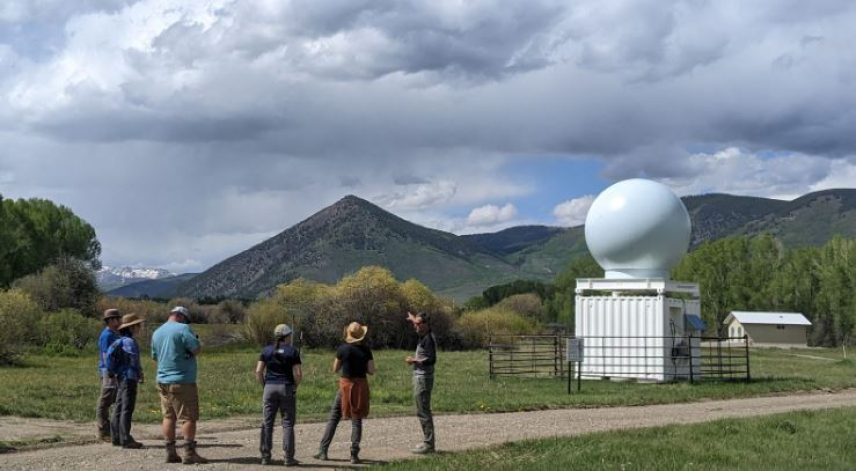 Five people stand near a large instrument that take measurements to help improve weather forecasts and runoff estimates. 