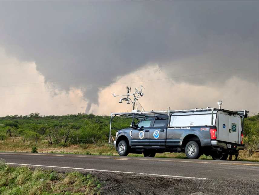 NOAA truck being used for field research in May 2024 in Oklahoma, as a tornado crosses a field in the distance.