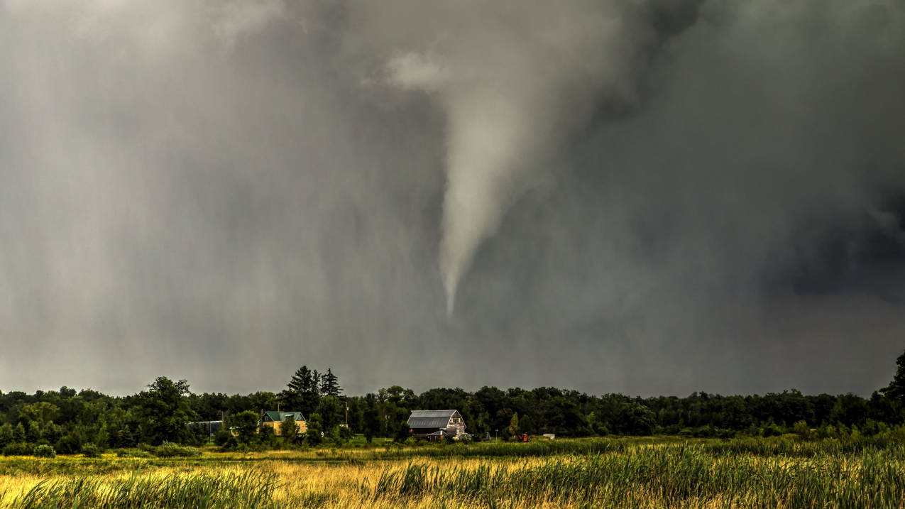 A storm with a condensed funnel cloud that is not touching the ground. The funnel cloud appears to be poised over a rural home.