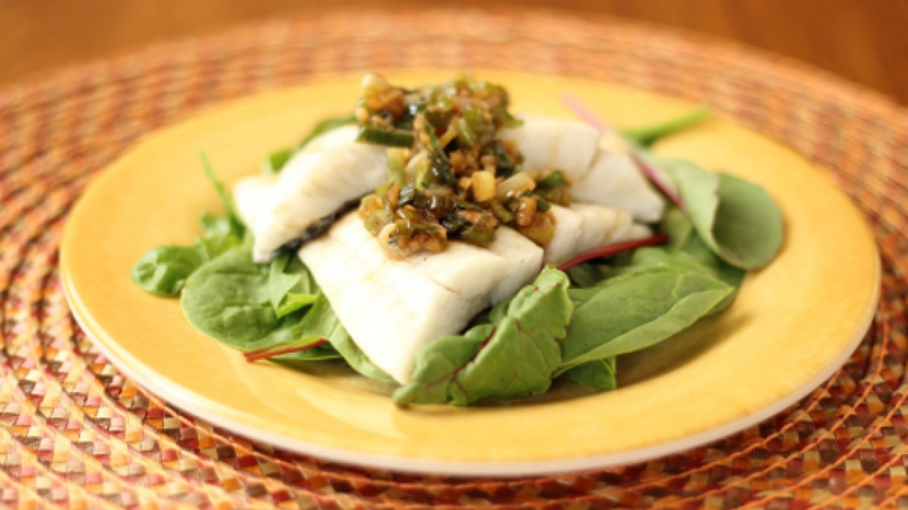 A beautifully plated seafood dish of white fish on a bed of leafy green bibb lettuce and topped with a chopped vegetable chutney.