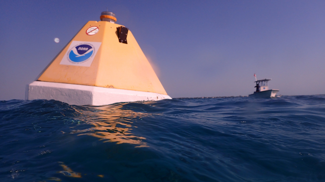 A NOAA buoy floats in the ocean with a vessel nearby.