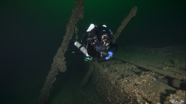 Photo of a diver examines the Great Lakes schooner St. Peter. One of Lake Ontario National Marine Sanctuary's most-visited, recreationally-accessible shipwrecks, St. Peter was carrying coal when it sank during a Lake Ontario storm in 1898.