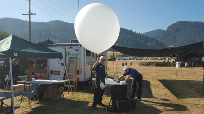 Incident Meteorologists (IMETs) Phil Manuel and Scott Weishaar prepare to launch a weather balloon on the Stouts Creek Fire near Canyonville, Ore. August 16, 2015. IMETs depend on data from weather balloons and many other sources to develop tailored forecasts critical to fighting wildfires. 
